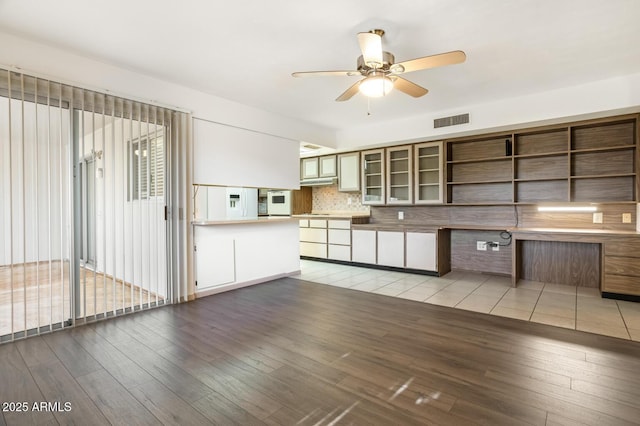 kitchen with backsplash, white fridge with ice dispenser, ceiling fan, kitchen peninsula, and light wood-type flooring