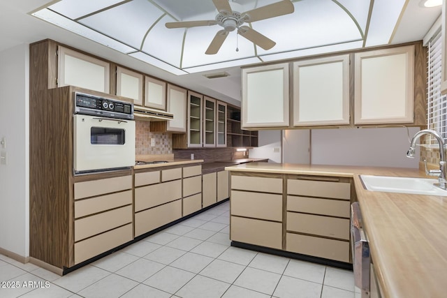 kitchen with sink, oven, decorative backsplash, light tile patterned floors, and ceiling fan