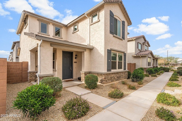 view of front facade featuring stone siding, fence, and stucco siding