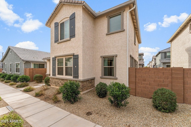 view of home's exterior with stone siding, fence, and stucco siding