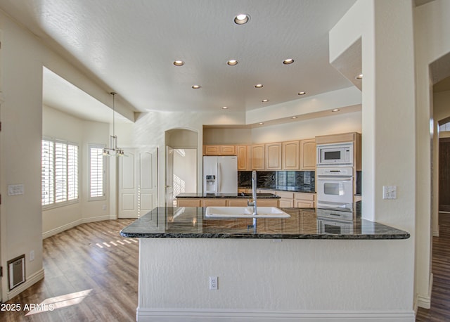 kitchen with white appliances, light brown cabinets, arched walkways, decorative backsplash, and light wood-type flooring