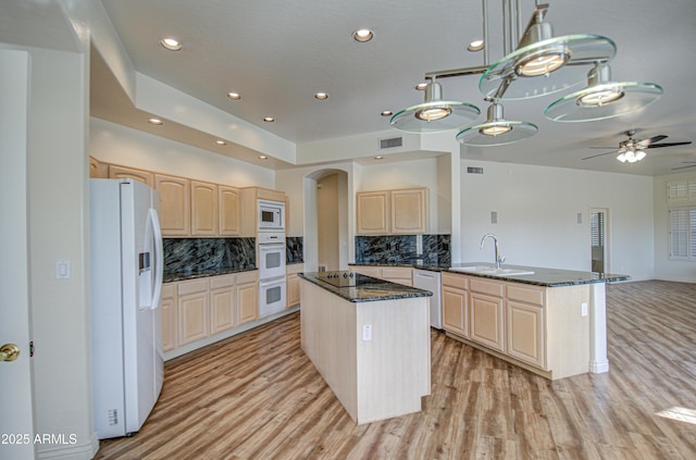 kitchen featuring light brown cabinets, white appliances, a kitchen island, and a sink