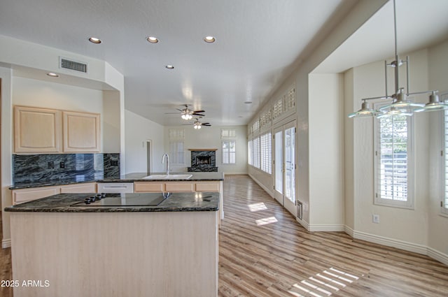 kitchen featuring light brown cabinets, visible vents, a fireplace with raised hearth, a sink, and black electric stovetop