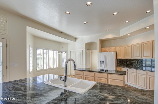 kitchen with light brown cabinetry, a sink, backsplash, a kitchen island, and white refrigerator with ice dispenser