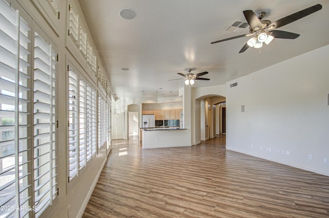 unfurnished living room featuring wood finished floors, visible vents, a ceiling fan, baseboards, and arched walkways