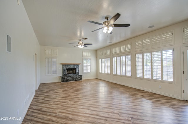 unfurnished living room with visible vents, wood finished floors, a premium fireplace, baseboards, and ceiling fan