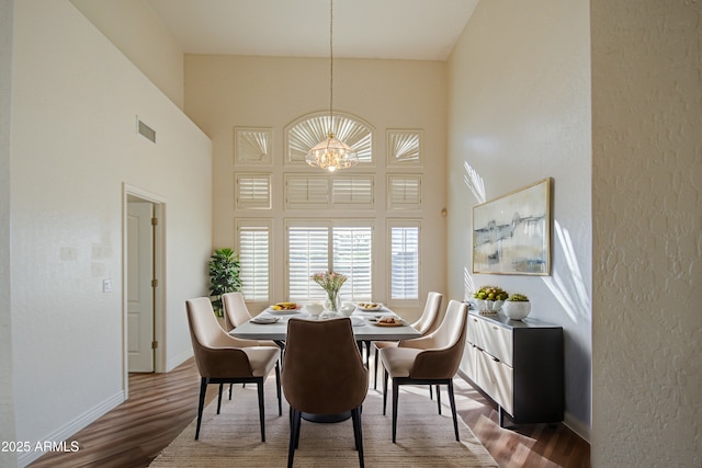 dining space featuring visible vents, a notable chandelier, wood finished floors, baseboards, and a towering ceiling