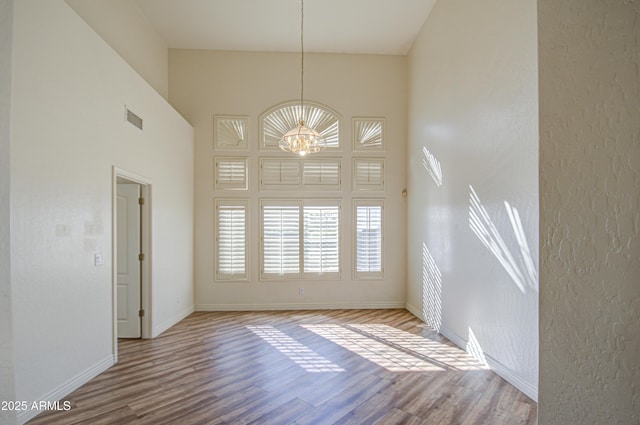 empty room with a notable chandelier, baseboards, visible vents, and wood finished floors