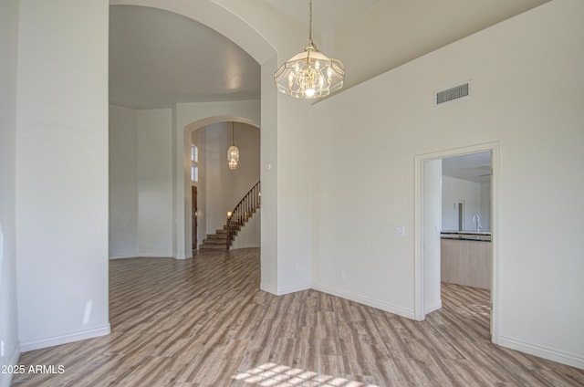 spare room with visible vents, wood finished floors, arched walkways, baseboards, and a chandelier