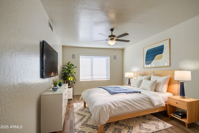 bedroom with wood finished floors, visible vents, and ceiling fan