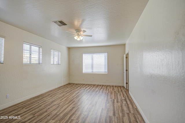 unfurnished room featuring visible vents, baseboards, ceiling fan, wood finished floors, and a textured ceiling