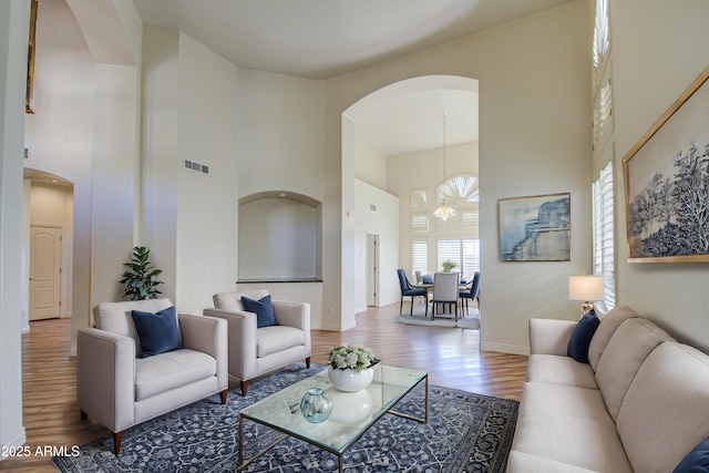 living area with arched walkways, visible vents, a towering ceiling, and wood finished floors