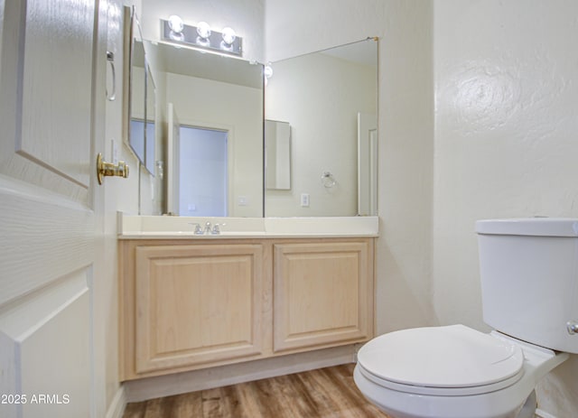 half bath featuring toilet, vanity, and wood finished floors