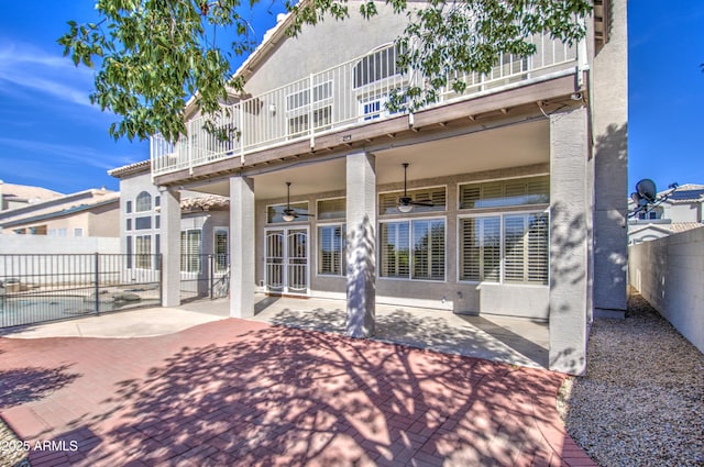 rear view of house featuring a balcony, a ceiling fan, a fenced backyard, stucco siding, and a patio area