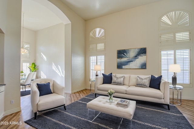 living area with light wood-style flooring, baseboards, arched walkways, and a towering ceiling