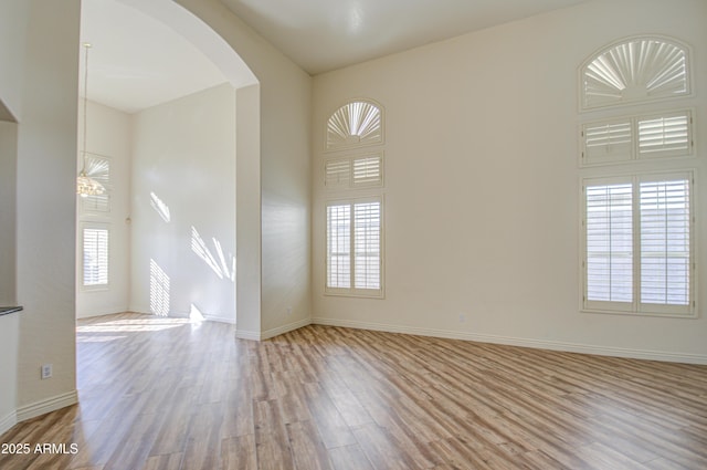 spare room with plenty of natural light, wood finished floors, arched walkways, and baseboards