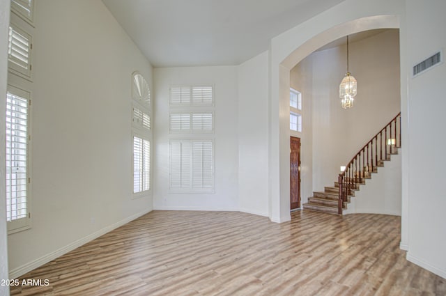 entryway with visible vents, arched walkways, light wood finished floors, a towering ceiling, and stairs