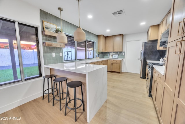 kitchen with visible vents, light wood finished floors, a peninsula, and stainless steel range with electric stovetop