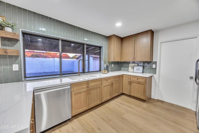 kitchen featuring light countertops, tasteful backsplash, a sink, light wood-style flooring, and dishwasher