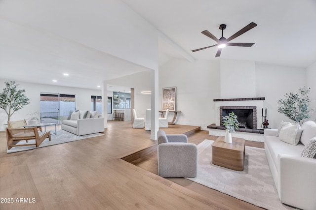 living room with ceiling fan, vaulted ceiling, wood finished floors, and a brick fireplace