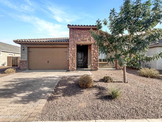 mediterranean / spanish home featuring decorative driveway, stucco siding, an attached garage, stone siding, and a tiled roof