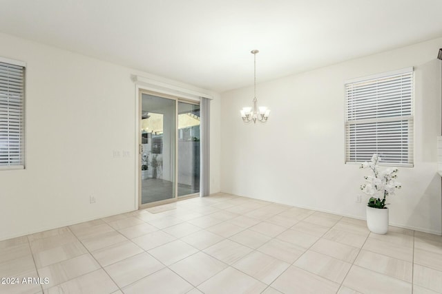 tiled spare room with a notable chandelier