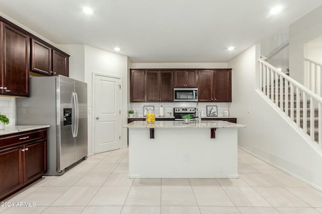 kitchen featuring a breakfast bar, backsplash, a kitchen island with sink, light stone countertops, and stainless steel appliances