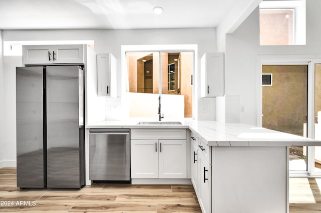 kitchen with sink, light wood-type flooring, kitchen peninsula, stainless steel appliances, and white cabinets