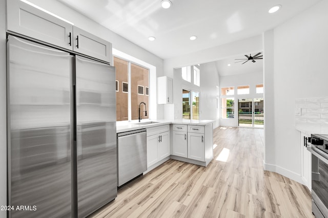 kitchen with kitchen peninsula, white cabinetry, light wood-type flooring, sink, and stainless steel appliances