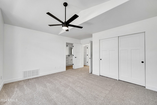 unfurnished bedroom featuring connected bathroom, light colored carpet, a closet, and ceiling fan