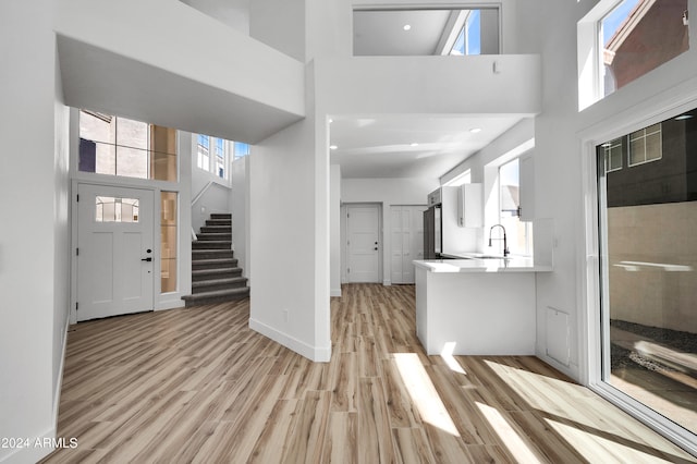 entryway with a healthy amount of sunlight, a towering ceiling, sink, and light wood-type flooring