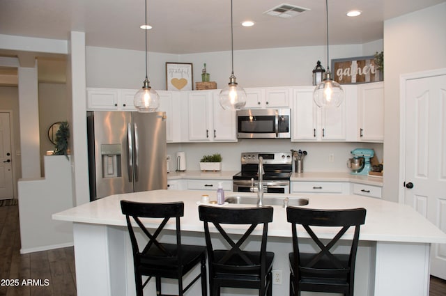 kitchen featuring appliances with stainless steel finishes, decorative light fixtures, a center island with sink, and white cabinets