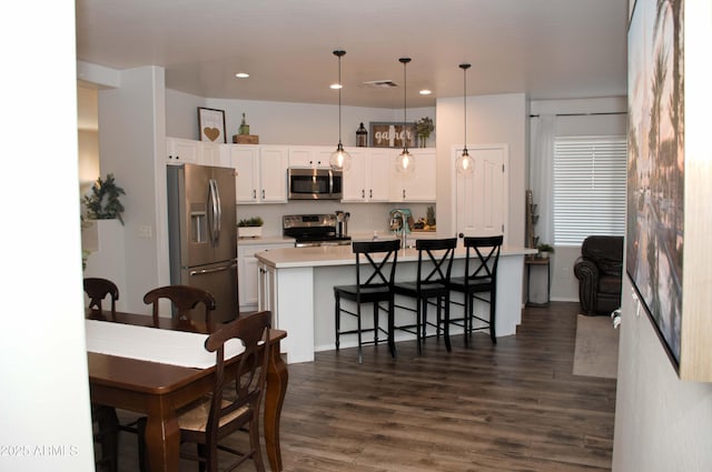 kitchen featuring appliances with stainless steel finishes, pendant lighting, white cabinets, a kitchen bar, and a center island with sink