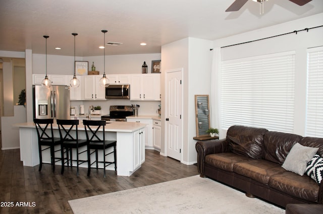 kitchen with a breakfast bar, appliances with stainless steel finishes, white cabinets, a center island with sink, and decorative light fixtures