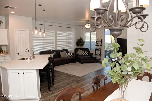 dining space featuring ceiling fan with notable chandelier, sink, and dark wood-type flooring