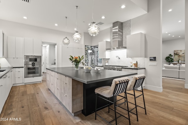 kitchen featuring wall chimney range hood, light hardwood / wood-style flooring, white cabinets, and a large island