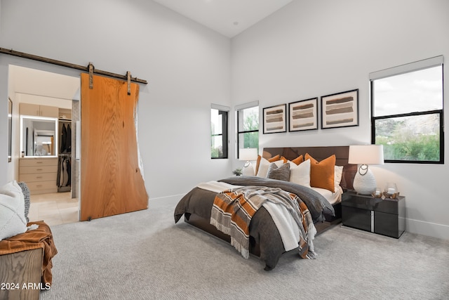 bedroom with a towering ceiling, a walk in closet, a barn door, and light colored carpet