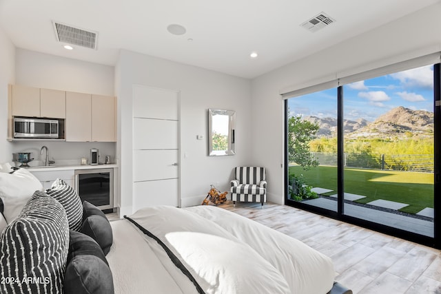 bedroom featuring wine cooler, access to exterior, light hardwood / wood-style flooring, a mountain view, and sink