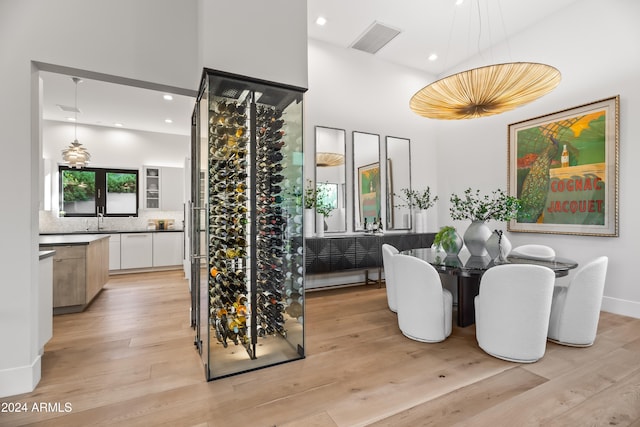 wine area featuring a towering ceiling, sink, and light wood-type flooring