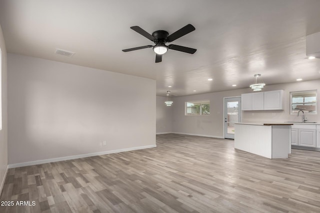 unfurnished living room featuring light wood-style flooring, baseboards, visible vents, and a sink