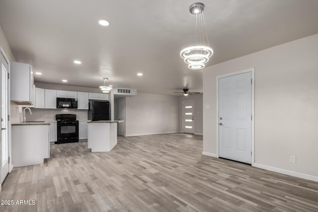 kitchen with visible vents, black appliances, open floor plan, white cabinetry, and a sink