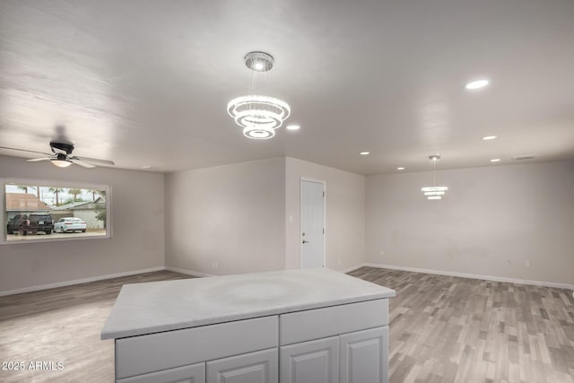 kitchen featuring light wood finished floors, baseboards, decorative light fixtures, open floor plan, and light countertops