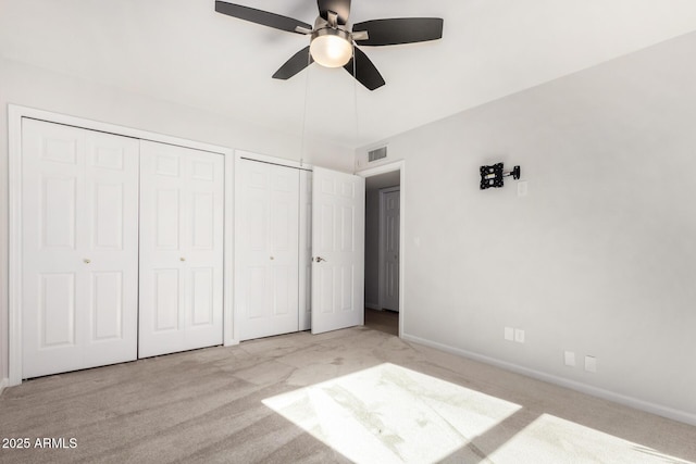 unfurnished bedroom featuring ceiling fan, multiple closets, and light carpet