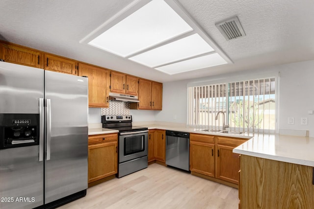 kitchen with appliances with stainless steel finishes, light wood-type flooring, decorative backsplash, a textured ceiling, and sink