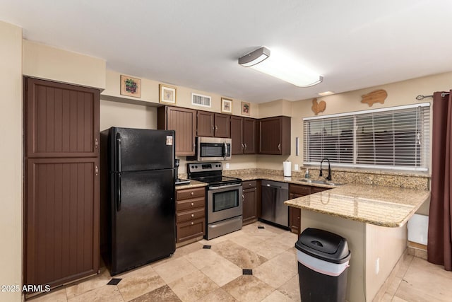 kitchen featuring sink, appliances with stainless steel finishes, dark brown cabinets, light stone countertops, and kitchen peninsula