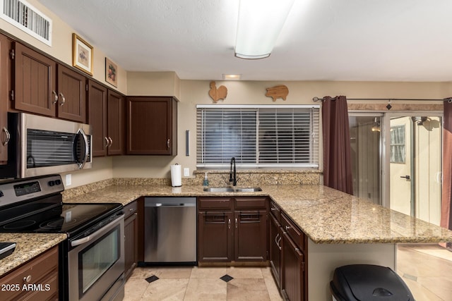 kitchen with sink, stainless steel appliances, dark brown cabinetry, light stone countertops, and kitchen peninsula