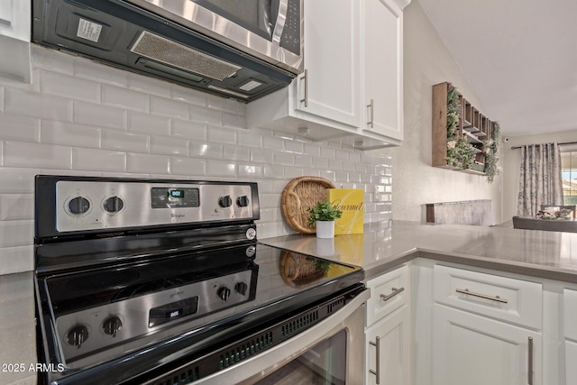 kitchen with appliances with stainless steel finishes, white cabinets, lofted ceiling, and decorative backsplash