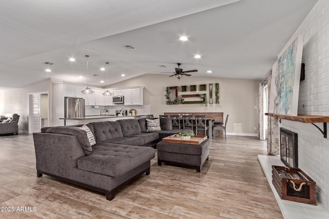 living room with a brick fireplace, ceiling fan, and vaulted ceiling