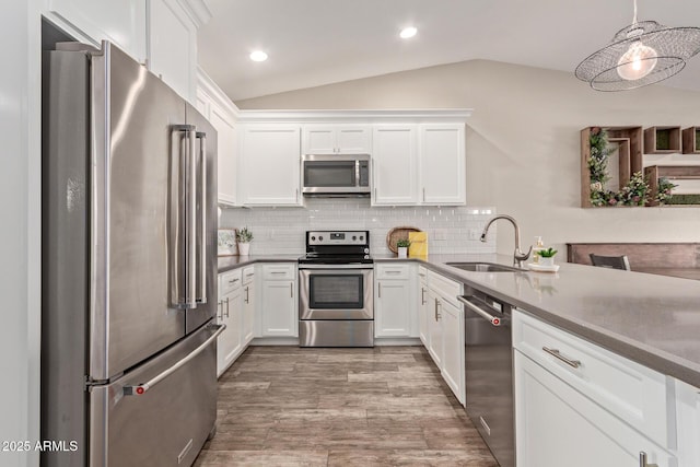 kitchen with hanging light fixtures, lofted ceiling, white cabinetry, appliances with stainless steel finishes, and sink