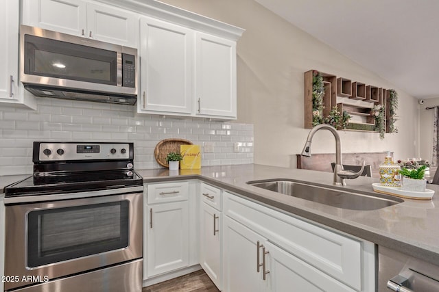 kitchen featuring vaulted ceiling, stainless steel appliances, light stone counters, sink, and white cabinetry